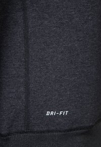 Primo piano di un tessuto grigio scuro con una cucitura verticale e il logo bianco "DRI-FIT" stampato vicino al bordo inferiore.