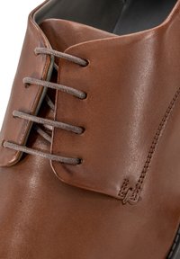 Scarpa in pelle marrone con punta arrotondata, dotata di lacci grigi e un sottile dettaglio di cucitura sulla parte superiore. Texture liscia e finitura lucida.