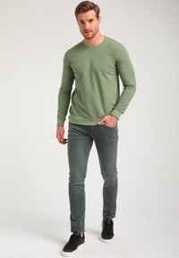 Sudadera de manga larga verde claro con patrón texturizado, cuello redondo y puños acanalados. Combinada con jeans gris ajustados y zapatillas negras.