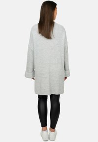 Cardigan oversized grigio chiaro in maglia con maniche lunghe, texture a coste e orlo grezzo; abbinato a leggings neri e sneakers bianche.