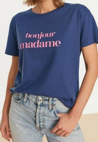 Navy sininen puuvillapaita, jossa on vaaleanpunaista tekstiä "bonjour madame". Lyhyet hihat, pyöreä kaula-aukko, rento malli, yhdistetty keveisiin farkkuihin.