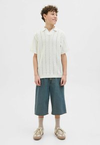 Vit stickad polo med vertikala öppningar, i kombination med löst sittande ljusblå jeansshorts. Avslutad med beige sneakers och ljusa strumpor.