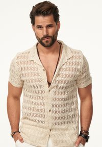 Beige, kurzärmeliges Häkelshirt mit Knopfleiste, das ein offenes Strickmuster, eine texturierte Webart und einen entspannten Kragen aufweist.