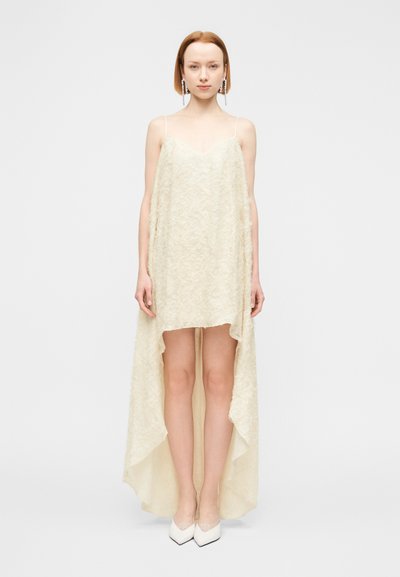 Robe ivoire évasée avec une texture en dentelle, dotée de bretelles fines et d'un ourlet asymétrique. Associée à des escarpins blancs à bout pointu.