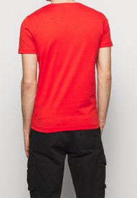 Camiseta roja de manga corta con cuello redondo, hecha de algodón suave, que presenta una textura lisa y un corte clásico. Se muestra la vista trasera.