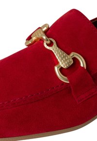 Red suede loafers featuring a gold decorative hardware accent and a rounded toe. The stitching is visible along the edges.