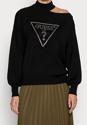 Pull noir avec col montant et une épaule dénudée, arborant un logo en triangle en strass argenté sur le devant. Texture douce, coupe ample.