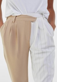 Plisserade byxor med en tan-sida och en vit-sida med vertikala ränder. Tillverkade av ett mjukt tyg, med sidfickor och en skräddarsydd passform.