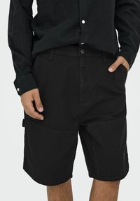 Zwarte cargo shorts van katoen, met meerdere zakken, een comfortabele pasvorm en subtiele stiksels. Gedragen met een bijpassend zwart shirt.