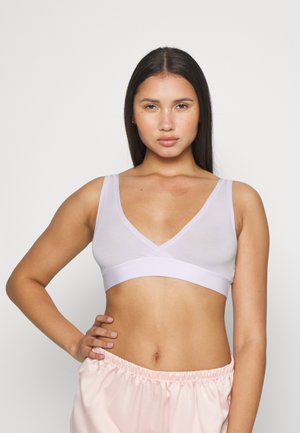 Bralette lilás claro feito de material transparente com um design de decote em V profundo e uma faixa elástica larga na parte inferior. Modelo vestindo calças rosa claro.