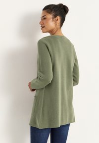 Långärmad, olivgrön stickad cardigan med texturerad yta och sidofickor, med en avslappnad passform och rund halsringning.