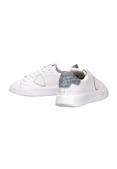 Deportivas blancas con una superficie de cuero suave, punta redonda y acentos de lentejuelas azules en el talón. Suela de goma texturizada.