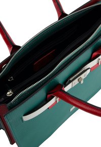 Turquoise leren handtas met rode handvatten, witte en rode vooraccent, en open bovenkant die meerdere met rits afgesloten compartments binnenin toont.