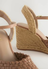 Wedge sandals with a woven raffia heel, tan leather straps, and a textured ankle strap. Features a smooth footbed with branding detail.