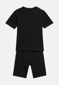 Μαύρο κοντομάνικο t-shirt με στρογγυλή λαιμόκοψη σε συνδυασμό με μαύρο σορτς μέχρι το γόνατο, απεικονίζεται από πίσω σε λευκό φόντο.