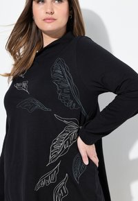 Zwarte longsleeve top met bladpatronen in blauwe en witte borduursels, met een relaxte pasvorm en een zachte, gladde textuur.