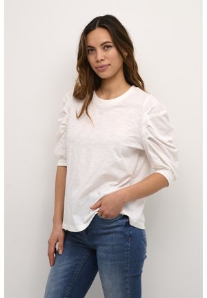 White, textured, crew-neck top with puff sleeves. Paired with blue denim jeans. The fabric appears soft and lightweight.
