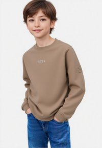 Felpa beige con scollo a girocollo e logo ricamato sottile. Maniche lunghe con polsini a costine, abbinata a jeans di denim blu.