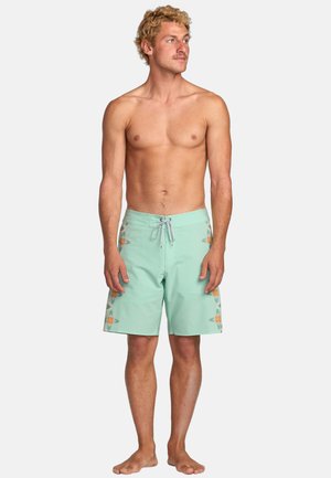 Pantaloni da bagno verde menta con motivi laterali arancioni e gialli. Presentano una vita regolabile con cordino e un tessuto liscio e leggero.