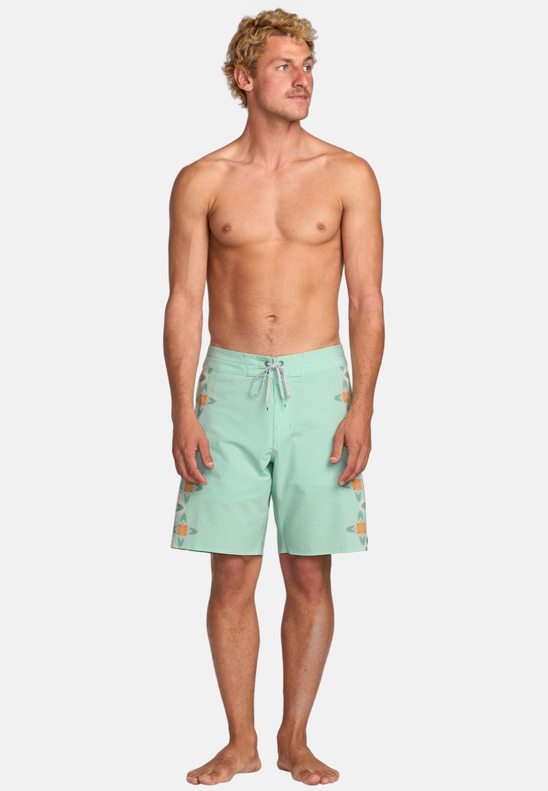 Pantaloni da bagno verde menta con motivi laterali arancioni e gialli. Presentano una vita regolabile con cordino e un tessuto liscio e leggero.