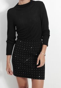 Haut noir à manches longues avec un col drapé associé à une jupe noire moulante ornée de clous en argent.