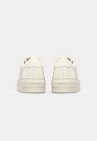 White leather sneakers with rounded toe, textured sole, and raised platform. Laces loop through eyelets; brand logo embossed on the heel.