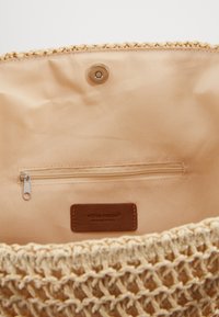 Vævet beige tote taske med en glat inderside, har en lynlåslomme og et brunt lædermærke. Åben top med struktureret design.