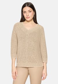Pull beige en tricot avec col en V, manches trois-quarts et motifs texturés. Tissu doux, léger avec une coupe décontractée.