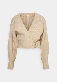 Beige ribbat stickad tröja med djup V-ringning, långa ärmar och ett midjebälte med en cirkulär ringbuckle i guldton.