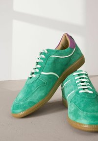 Baskets en suede vert avec des accents et des lacets blancs. Présentent un onglet de talon violet et une semelle en caoutchouc texturé pour une meilleure adhérence et un confort optimal.