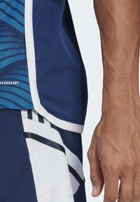 Granatowa sportowa koszulka z niebieskimi wzorzystymi akcentami, białą lamówką i materiałem odprowadzającym wilgoć, w połączeniu z granatowymi szortami z białymi i czarnymi paskami.