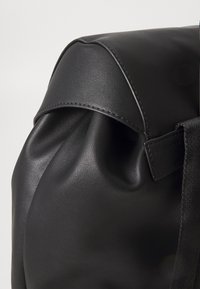 Black leather bag featuring a smooth, structured design with a folded top, stitched accents, and a durable textile strap.