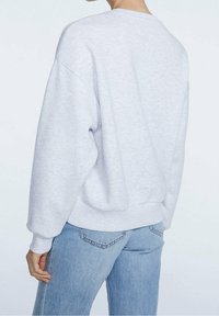 Grijze sweatshirt met een losse pasvorm, verlaagde schouders en geribbelde rand. Het stof lijkt zacht met een subtiele textuur. Gecombineerd met lichtblauwe jeans.