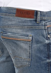 Traperice u srednje plavoj boji s trošenom teksturom, s smešnim kožnim logom "BLEND" i kontrastnim šavovima na džepovima.