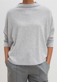 Šedý, měkký svetr s vysokým výstřihem a spadlými rameny. Má uvolněný střih a lemované manžety, doplněný o šedé kalhoty.