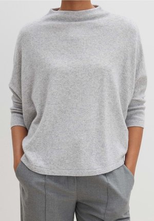 Grå, blød sweater med høj hals og droppede skuldre. Har en afslappet pasform og ribbede manchetter, parret med grå bukser.