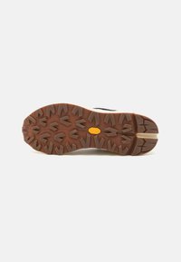 Trekking shoe outsole featuring a brown rubber tread with arrow patterns and a central logo. The design offers enhanced traction and stability.