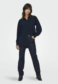 Navy blue long-sleeve shirt with button closure and a relaxed fit, paired with dark blue jeans and black heeled boots.