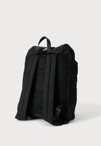 Μαύρο σακίδιο από ύφασμα με ενισχυμένη πλέκτη επένδυση στην πλάτη, ρυθμιζόμενους ιμάντες, χειρολαβή στην κορυφή και μινιμαλιστικό σχέδιο με λεπτομέρεια λογότυπου.