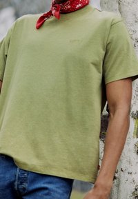 T-shirt en coton vert olive avec un col rond et des manches courtes, arborant un petit logo Levi's en relief sur la poitrine et associé à un jean bleu.