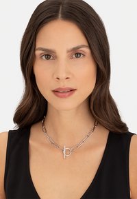 Silberne Metallkette mit länglichen Gliedern und einem kreisförmigen Toggle-Verschluss, die ein minimalistisches Design und eine polierte Oberfläche zeigt.