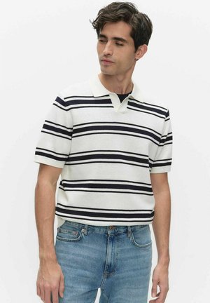 Jonge man met een wit poloshirt met korte mouwen en zwarte horizontale strepen en een blauwe spijkerbroek, lichtjes opzij kijkend.