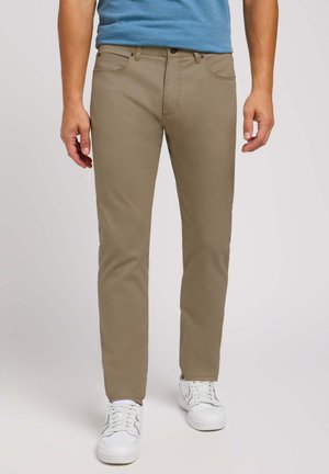Khaki-Hosen mit slim fit, Fünf-Taschen-Design und genähten Details, kombiniert mit weißen Sneakern und einem blauen T-Shirt.