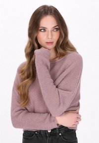 Lichtroze gebreide trui met een textuurpatroon, wijde halslijn en lange mouwen. Gestyled met zwarte high-waisted jeans.