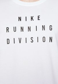Camiseta blanca con letras en bloque negras que dicen "DIVISIÓN DE CORRER NIKE". Cuenta con un cuello redondo y una textura de algodón suave. Diseño simple.