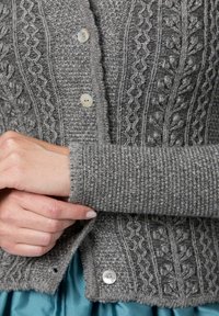 Grauer, gestrickter Cardigan mit strukturierten Mustern, ausgestattet mit sechs Knöpfen und gerippten Bündchen. Weiches Material mit verschiedenen Nähdetails.
