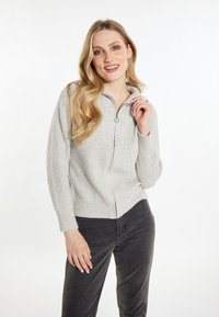 Maglione grigio chiaro con zip, texture a costine e colletto alto. Presenta maniche lunghe e un design aderente, abbinato a pantaloni grigio scuro.