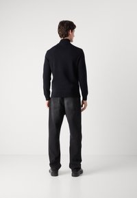 Marineblå strikkegenser med høy krage, kombinert med svarte denimjeans. antrekket har et enkelt, strømlinjeformet design og avslappet passform.