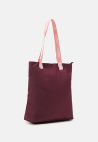 Bolsa tote de color granate hecha de tejido resistente al agua; cuenta con asas largas de color rosa con el logo "PUMA"; textura suave; diseño minimalista.