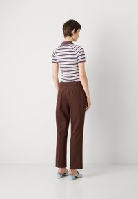 Polo a strisce con maniche corte bianco e marrone, abbinato a pantaloni marroni su misura e mule con tacco blocco blu. Vista posteriore.